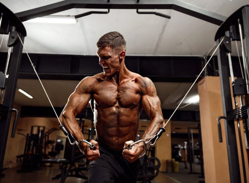 En vältränad man utför cable cross i ett gym.