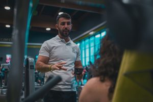 En personlig tränare instruerar en klient på ett gym med en mobiltelefon i handen.